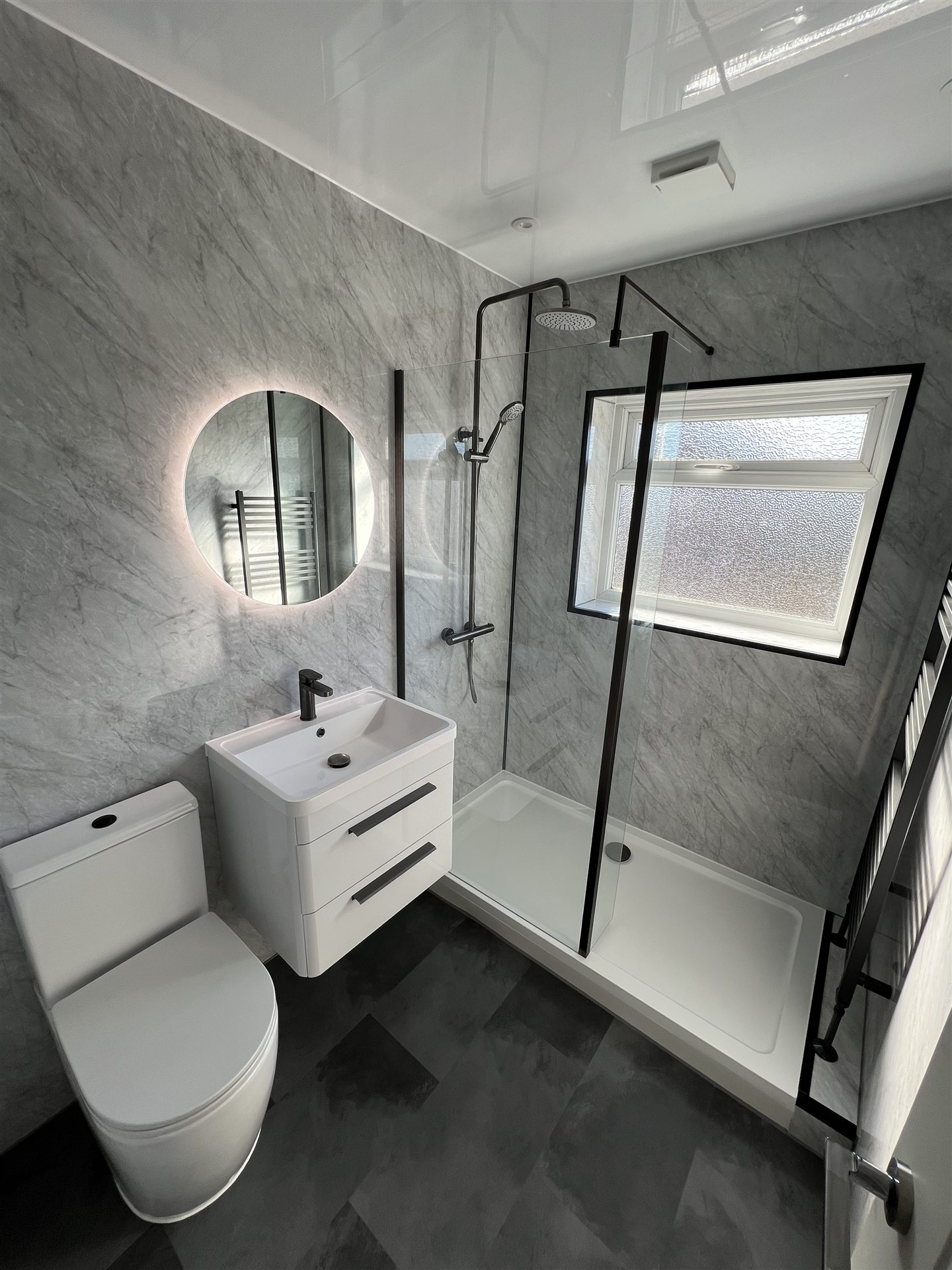 Marble-effect bathroom with backlit circular mirror and matte black fittings