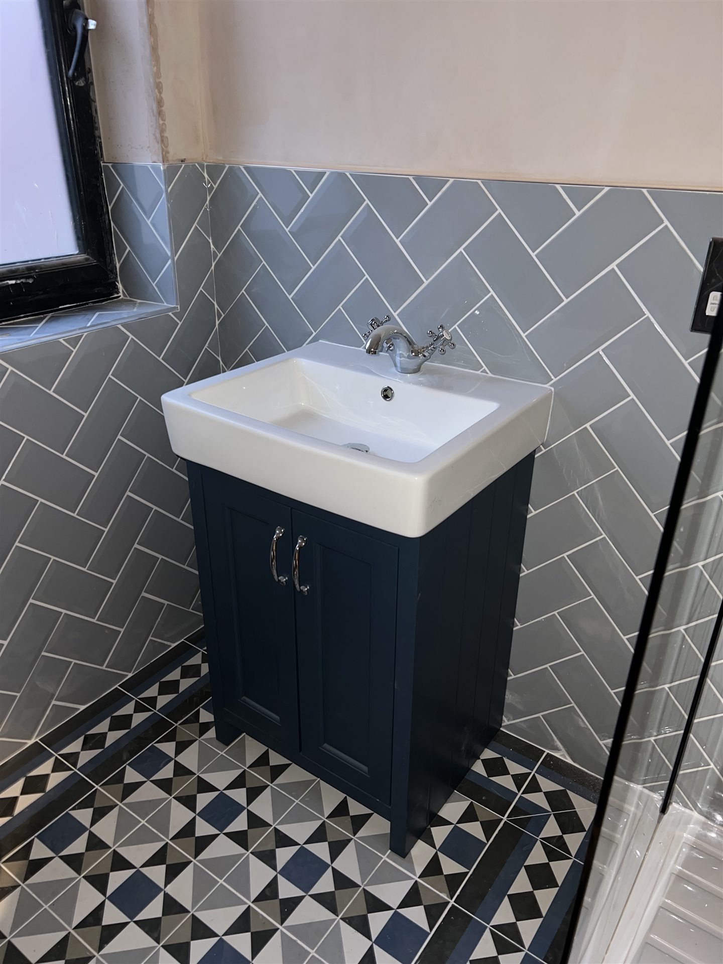 Herringbone tile bathroom with navy vanity unit and patterned floor